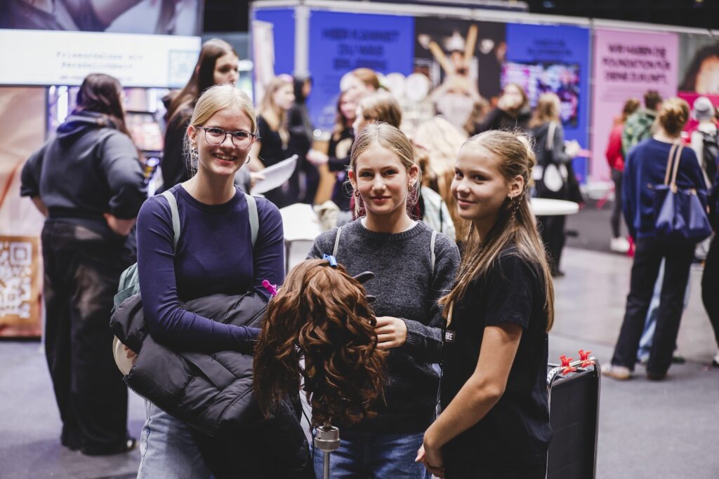 Drei Jugendliche Frauen posieren mit einem Übungskopf am Vorarlberg hat Style Stand auf der i-Messe 2025.