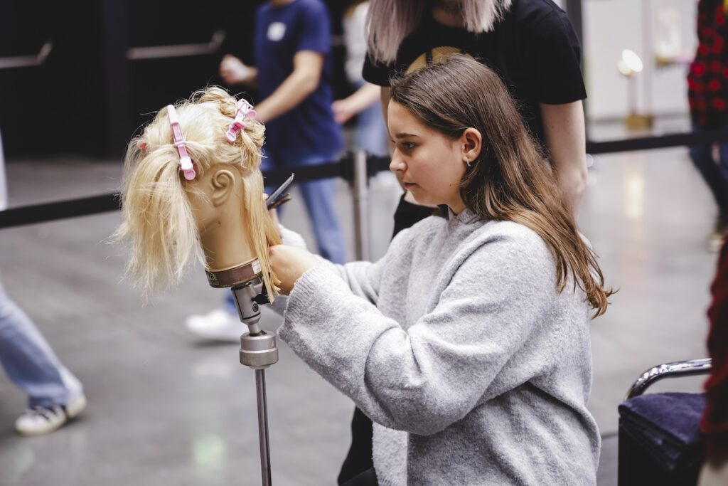 Schülerin übt das Schneiden an einem Übungskopf am Stand von Vorarlberg hat Style auf der i-Messe 2025.